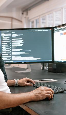 Ein Mitarbeiter sitzt vor zwei Computerbildschirmen und arbeitet konzentriert